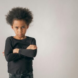 Portrait of a young child with crossed arms and a serious expression in a studio setting.