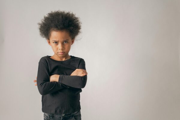 Portrait of a young child with crossed arms and a serious expression in a studio setting.