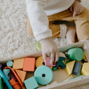 Child playing with vibrant wooden blocks on carpet, enhancing learning through play.