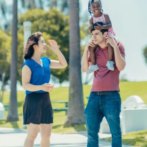 Multicultural family having fun outdoors. Father carrying daughter, mother smiling.
