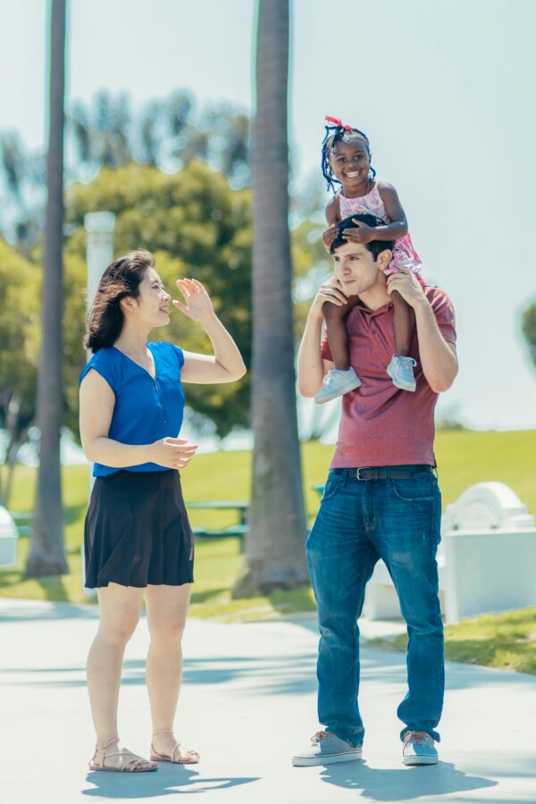 Multicultural family having fun outdoors. Father carrying daughter, mother smiling.